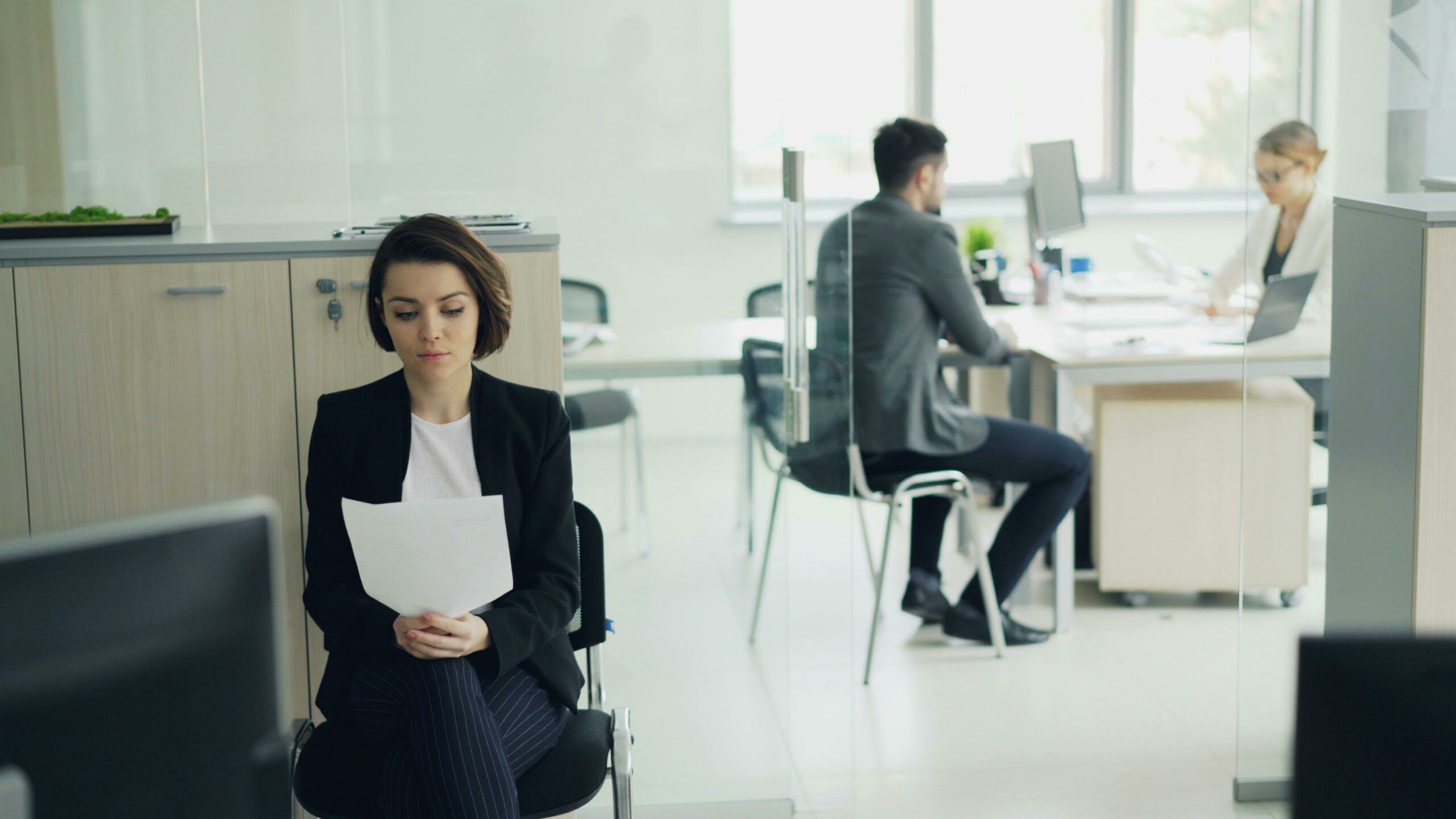 Business professionals working in a modern office setting with focus on a seated woman.